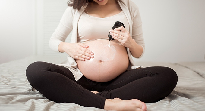 Pregnant woman applying moisturizer cream on belly