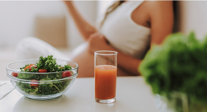 Pregnant woman with glass of orange juice and salad.
