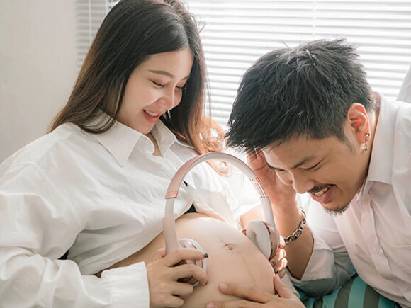 pregnant woman and her husband are holding headphones on tummy